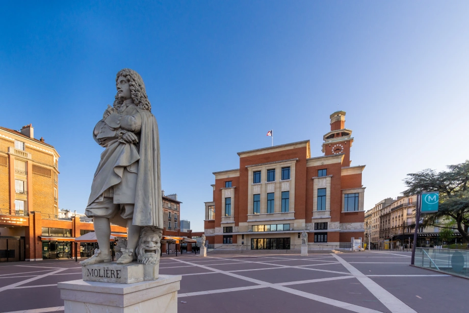 Statue de Molière au centre d'une place publique avec bâtiments historiques et théâtre en arrière-plan