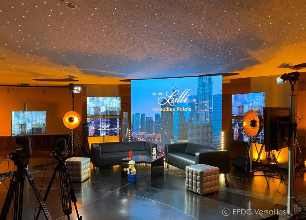 Studio moderne avec plafond étoilé orange et bleu, écrans de projection grands formats, caméras professionnelles, projecteurs, fauteuils noirs, mobilier design, technologie audiovisuelle haute définition