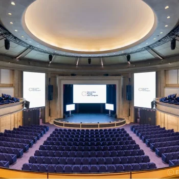 Amphithéâtre élégant avec sièges bleu marine, dôme lumineux, scène équipée d'écrans de projection, balcons latéraux, architecture moderne et raffinée