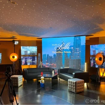 Studio moderne avec plafond étoilé orange et bleu, écrans de projection grands formats, caméras professionnelles, projecteurs, fauteuils noirs, mobilier design, technologie audiovisuelle haute définition